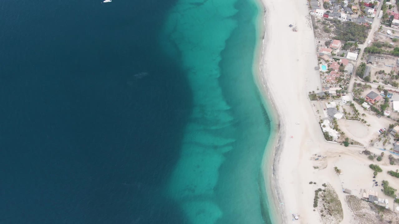 Aerial shoreline view with clear shallow water and beach buildings at the edge.