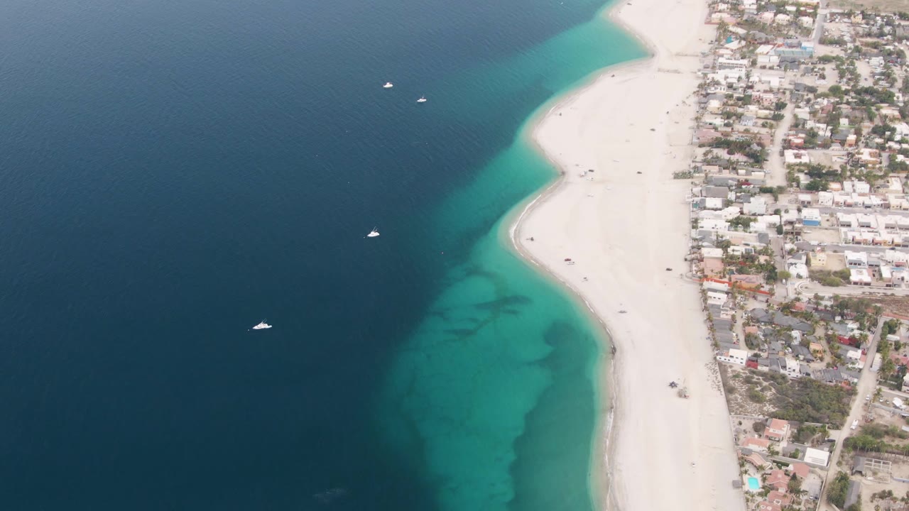 White beach and coastal homes beside dark blue ocean and turquoise shallows.