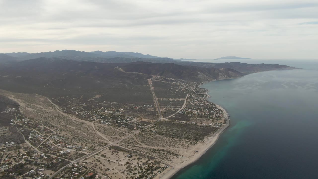 Drone view of beach town, coastal roadways, ocean, and distant hills.