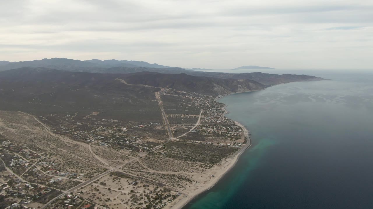 Aerial view of sandy coastline, ocean, town roads, and mountains