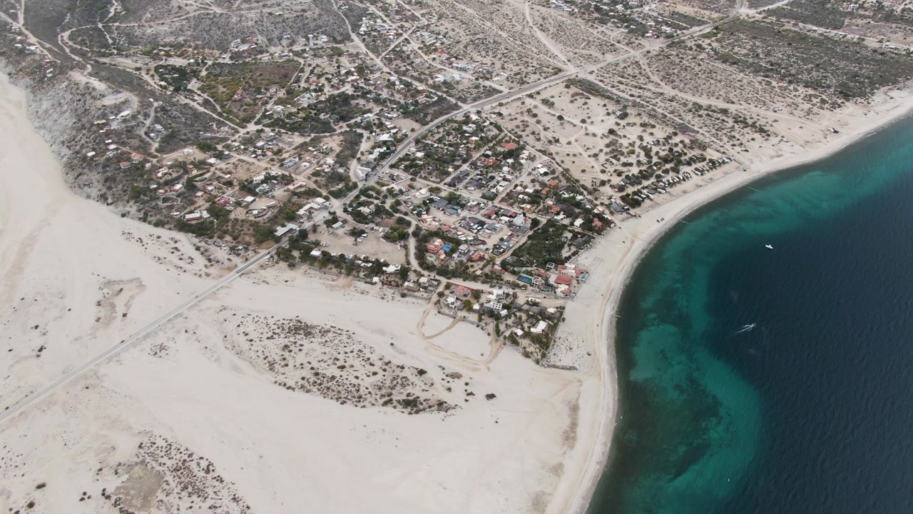 Aerial coastline with sandy foreground, homes, roads, and ocean edge