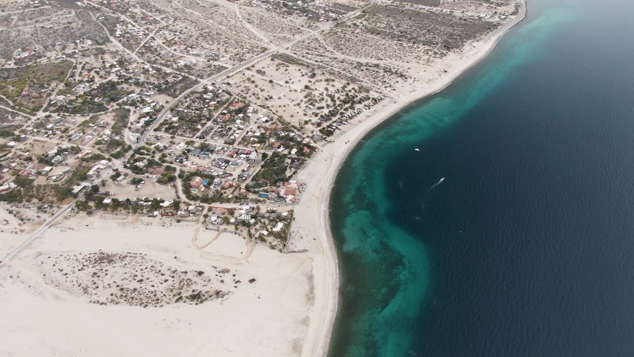 Drone view of a curved beach beside homes and turquoise ocean.