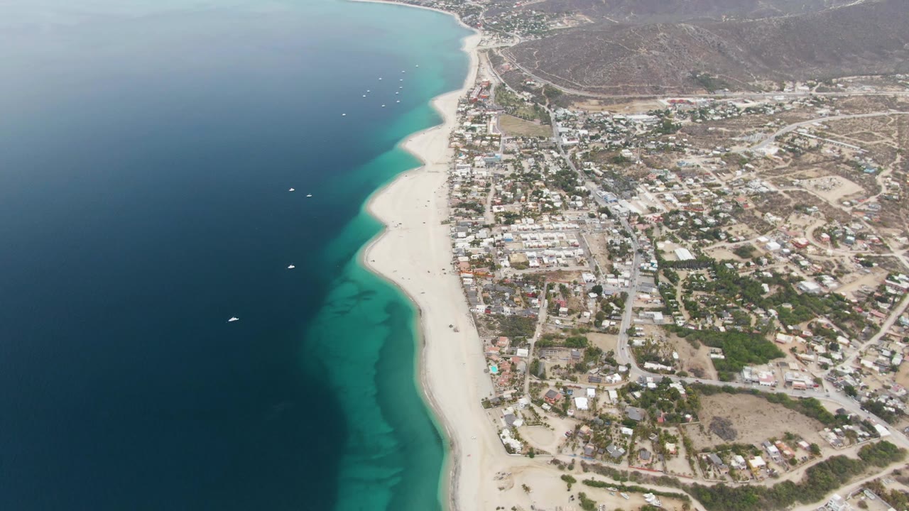 Drone view of coastal town beside a long white beach and blue water.
