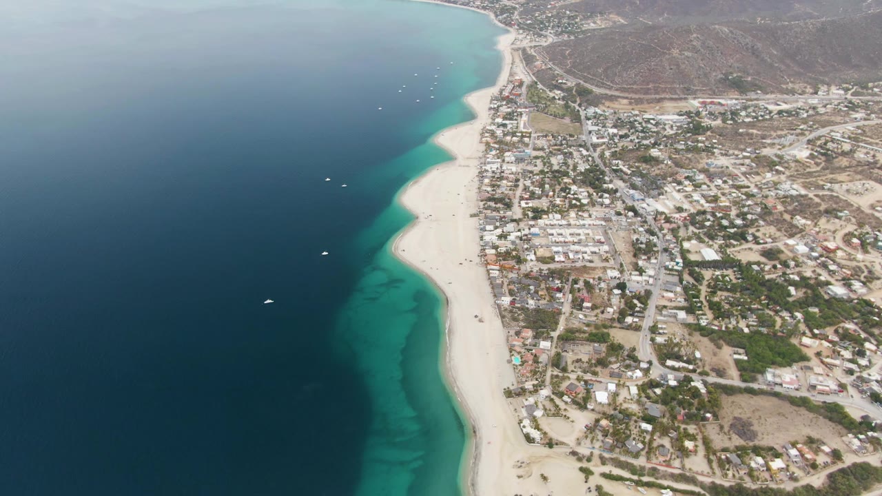 Drone view along turquoise shoreline beside town buildings