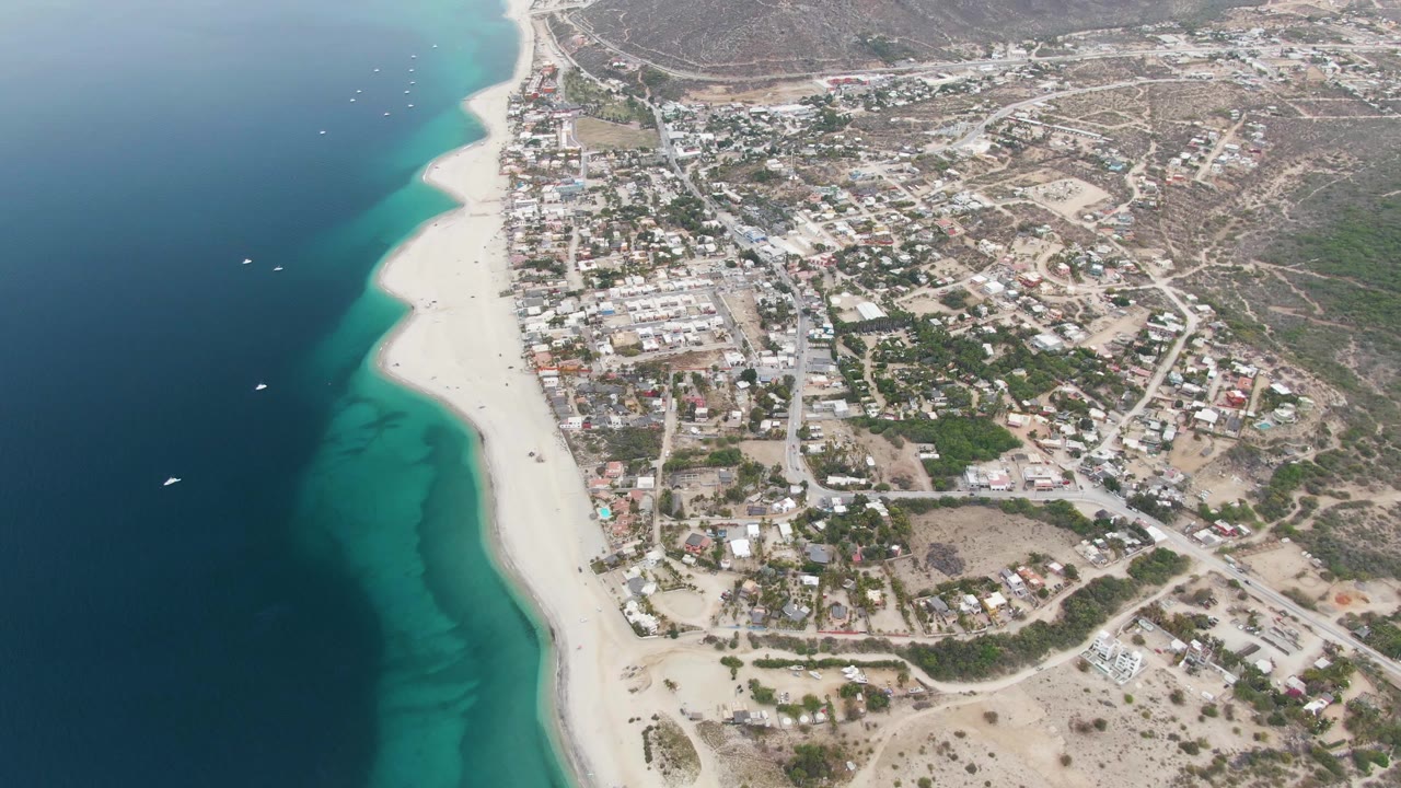 Drone view of turquoise shoreline beside a coastal settlement.
