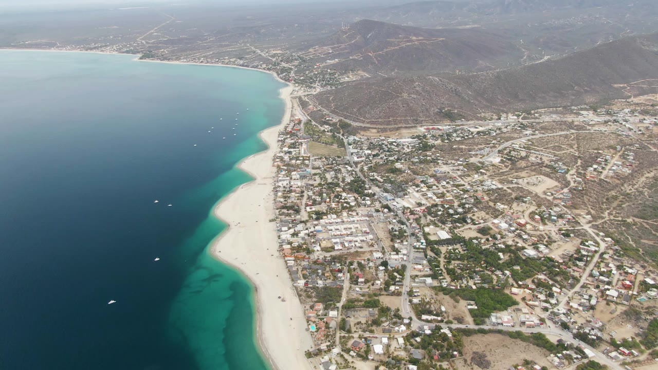Aerial coastline view with ocean, sandy beach, town blocks, and dry mountains.