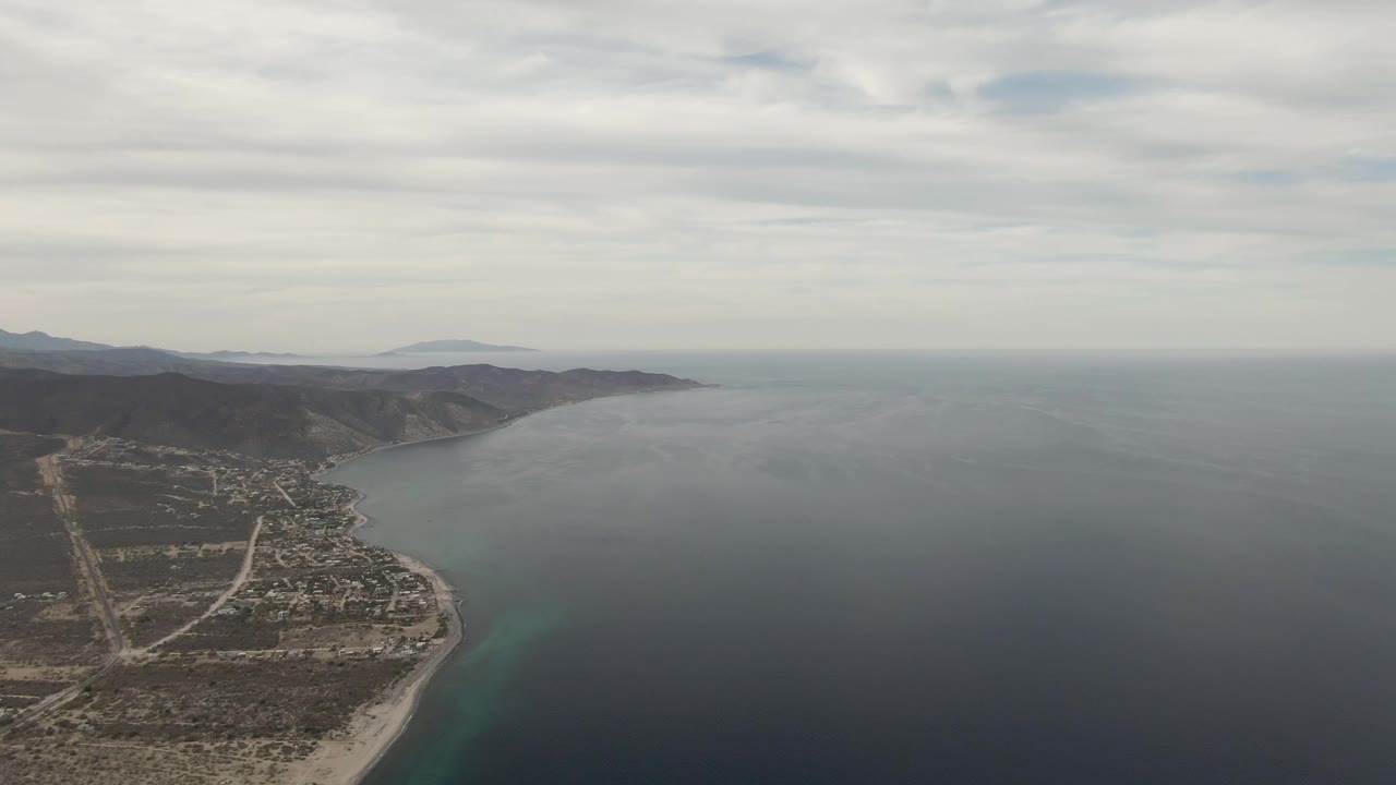 Aerial coastline with town, sandy shore, ocean, and overcast sky.