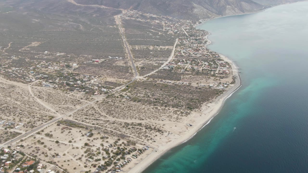 Drone view of a coastal town beside a pale beach and blue-green ocean.