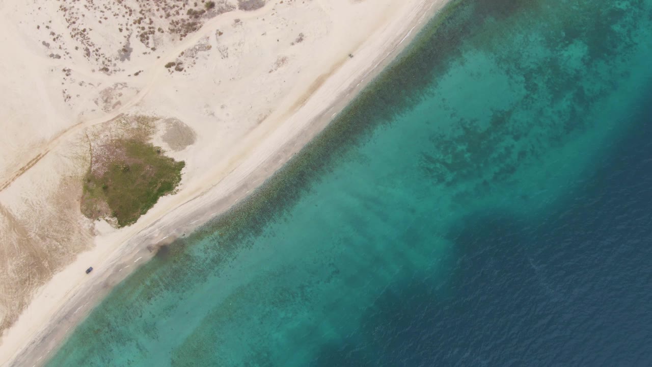 Overhead view of a sandy coastal road beside turquoise water.