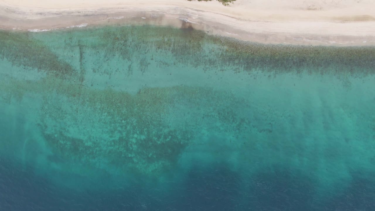 Overhead frame of Los Barriles shoreline with pale sand at the top, clear turquoise shallows, darker seabed patches, deeper blue water below, and no visible people.