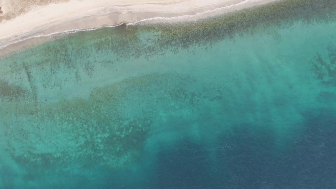 Overhead view of white sand and turquoise ocean shallows.