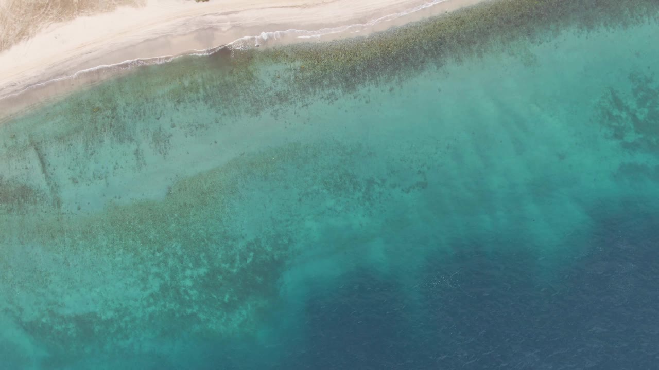 Aerial frame from Los Barriles with the pale beach curving across the top, translucent green-blue shallows through the center, and no visible people.