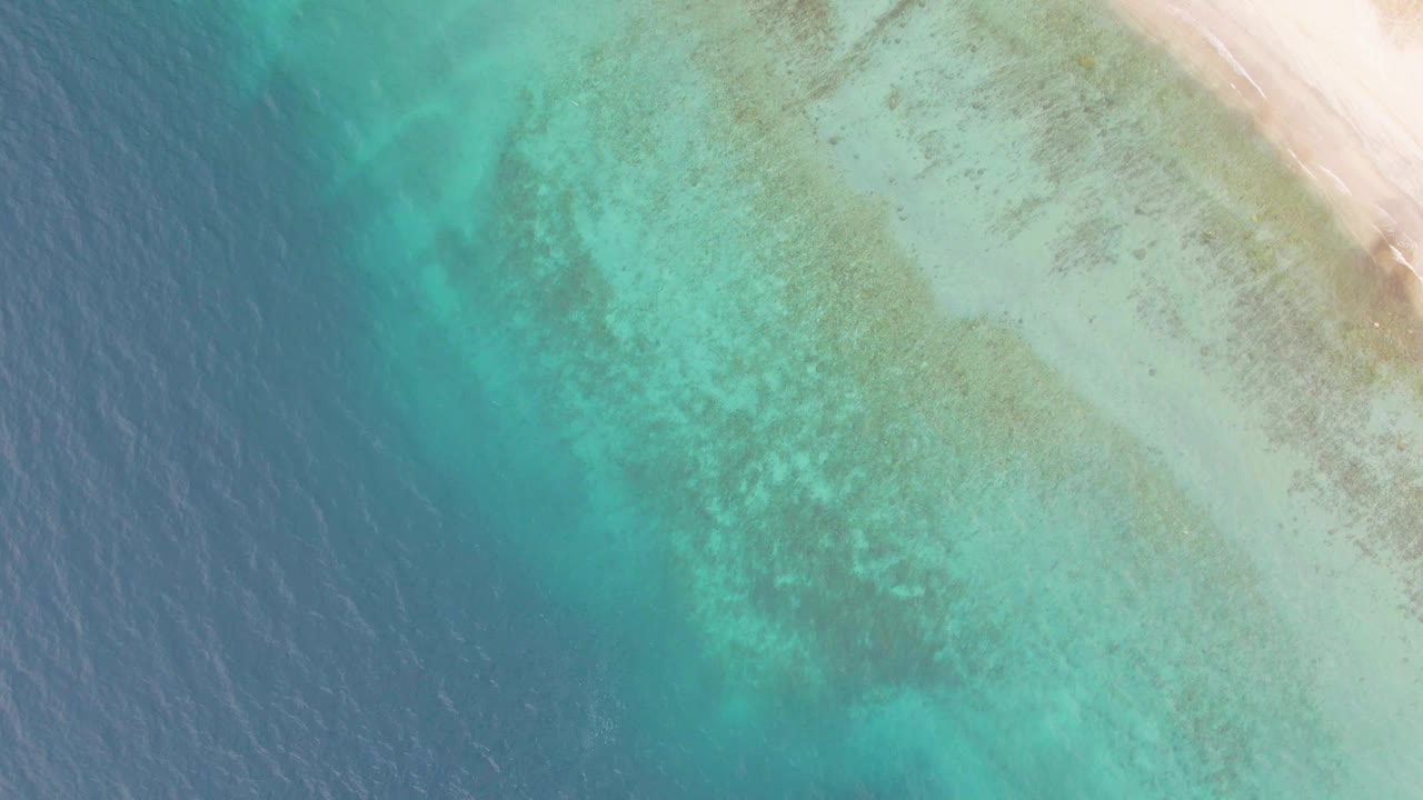 Overhead view of Los Barriles turquoise shallows grading into deeper blue water beside a pale sandy beach, with no visible people.