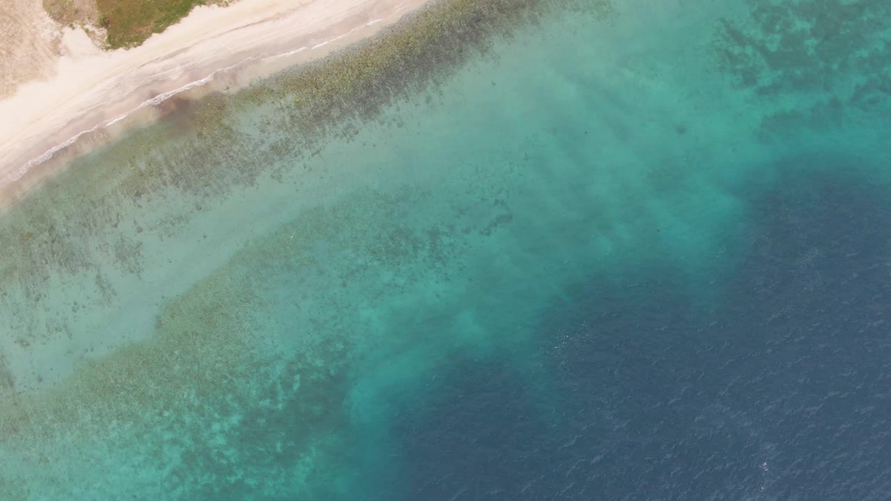 Overhead view of Los Barriles shoreline with pale sand at the upper left, turquoise shallows across the center, deeper blue water to the right, and no visible people.