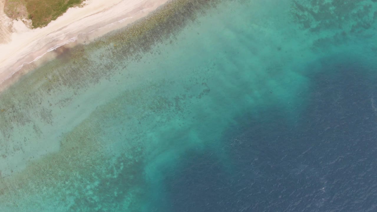 Los Barriles beach remains in the upper left while clear turquoise water reveals darker seabed texture across the middle and deep blue ocean fills the right, with no visible people.