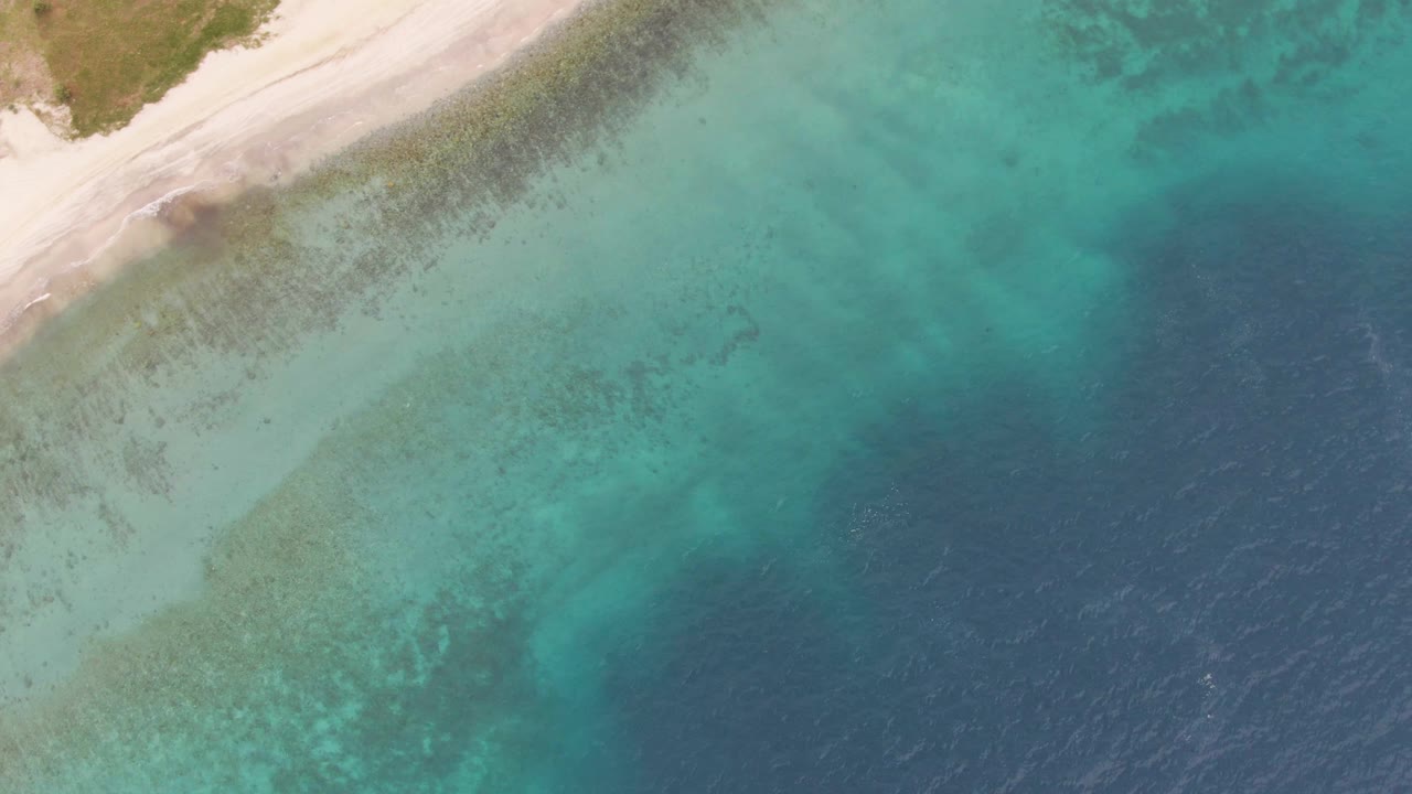 Aerial frame over Los Barriles showing a diagonal sandy beach at the upper left, broad turquoise shallows in the center, and a darker blue water band on the right, with no visible people.