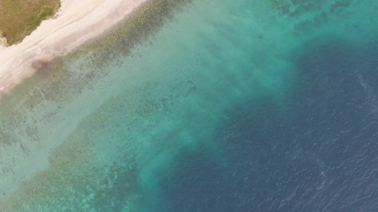 Close overhead view of beach edge, clear green-blue water, and open sea.