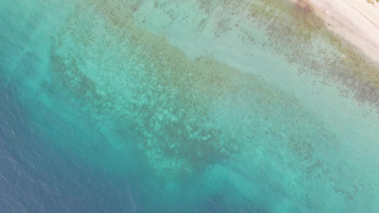 Top-down Los Barriles view with pale beach at the upper right, mottled seabed visible through turquoise shallows, darker water at the lower edge, and no visible people.