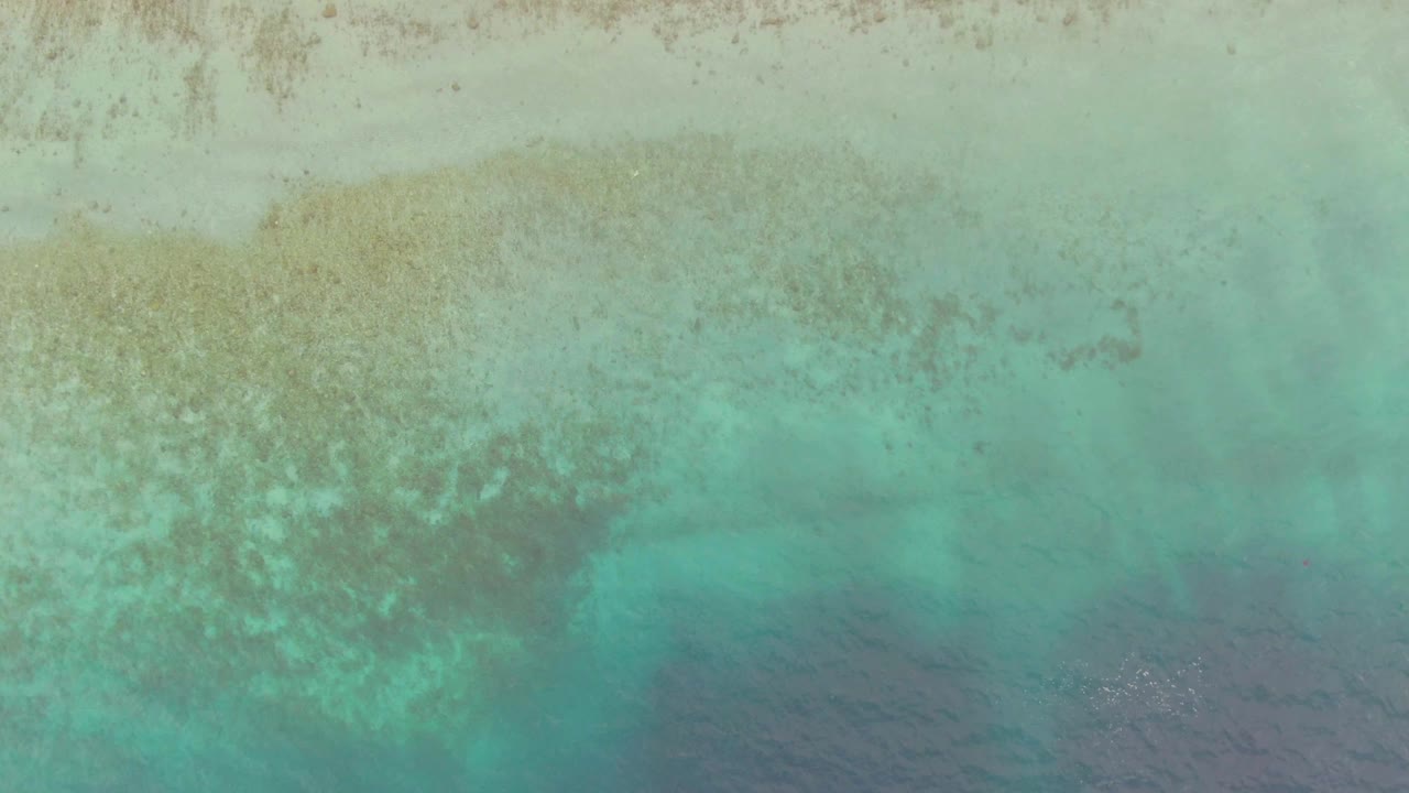 Overhead turquoise shallow water with pale sand and darker ocean at the bottom edge.