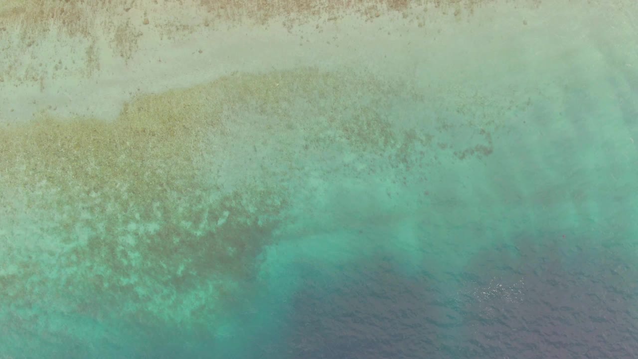 Aerial frame from Los Barriles, Mexico with broad pale sand showing through turquoise shallows, darker water at the bottom, faint surface texture, and no visible people.