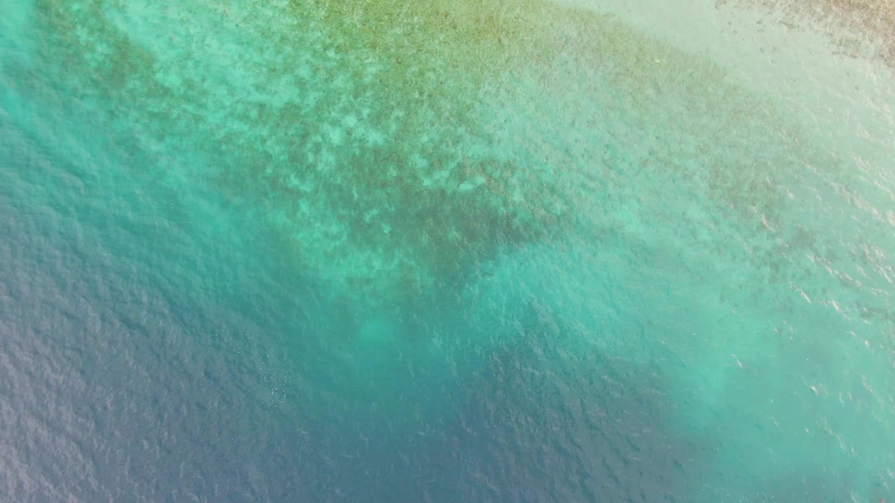 Turquoise sea surface in Los Barriles, Mexico, with pale shallow sand at the top edge, darker coral shapes below, and no visible people.