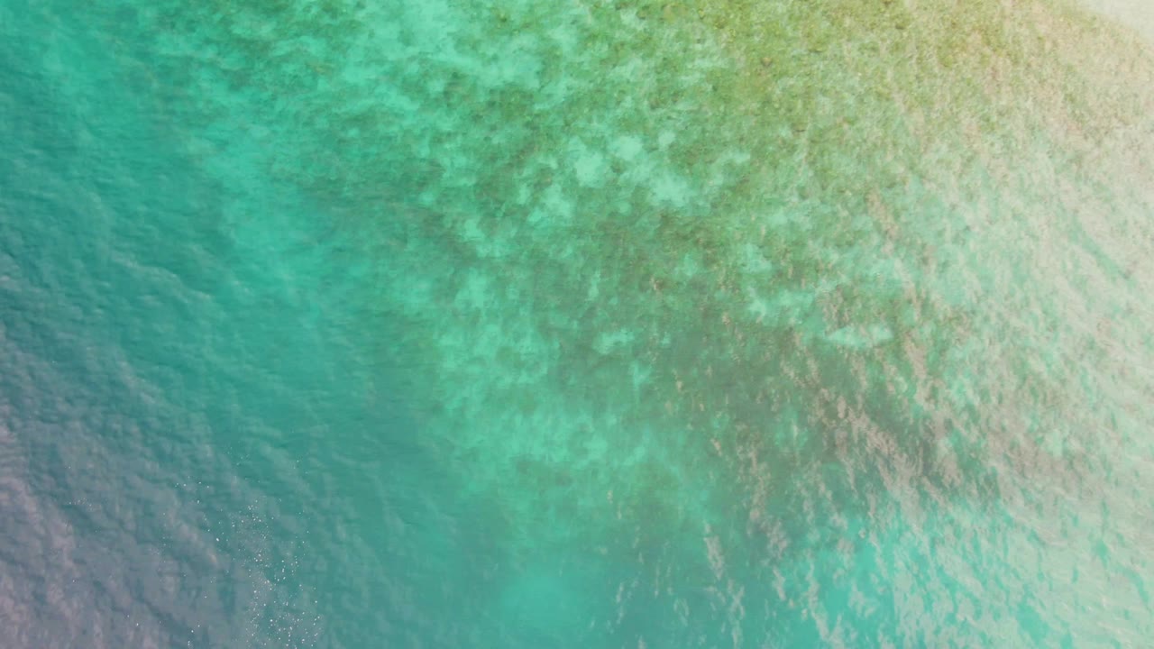 Aerial view of turquoise water in Los Barriles, Mexico, showing mottled darker seabed areas beneath the surface and no visible people.