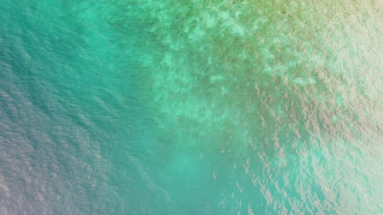 Clear blue-green coastal water in Los Barriles, Baja California Sur, with darker patches at left and a brighter rippled area toward the right, with no visible people.