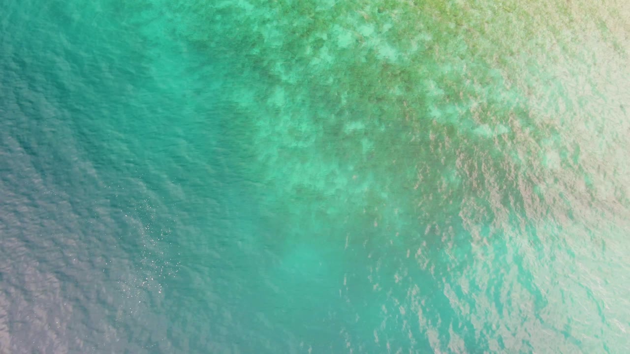 Straight-down aerial view of turquoise water in Los Barriles, Baja California Sur, with pale sunlight on the right side and darker blue-green water at left, with no visible people.