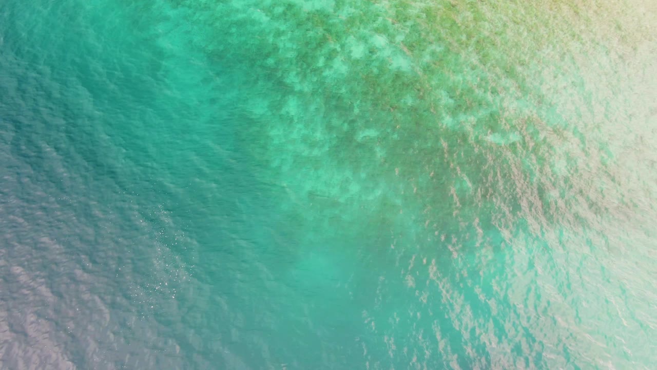 Shallow turquoise water in Los Barriles, Baja California Sur, seen from above with a broad darker area at lower left and pale rippled water at right, with no visible people.