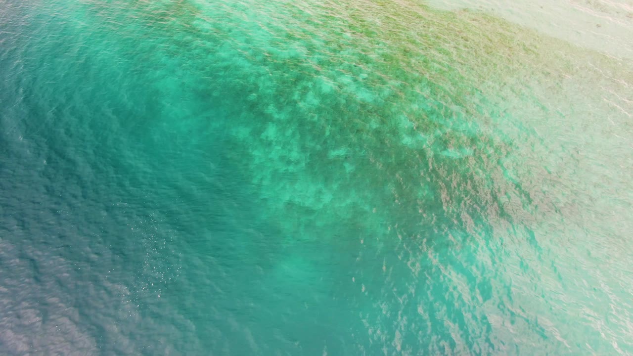 Overhead view of turquoise ocean water in Los Barriles, Baja California Sur, with pale submerged formations, darker teal water at lower left, and no visible people.