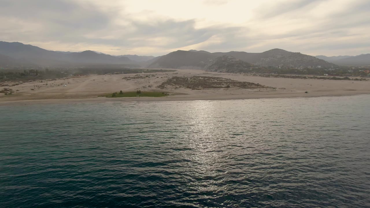 Second frame shows a wider band of reflective ocean below the sandy Los Barriles shoreline and layered mountains, with no visible people.