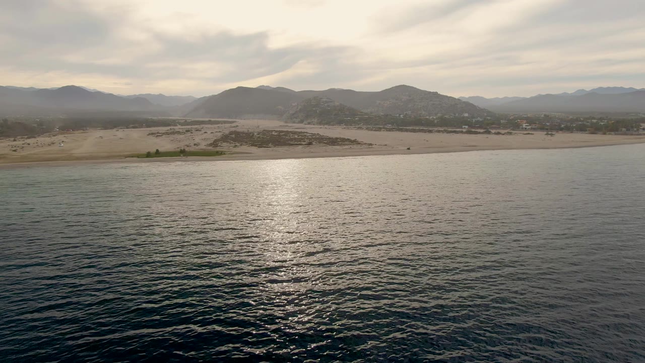 Cloudy coastal landscape with reflective ocean and mountains behind the beach