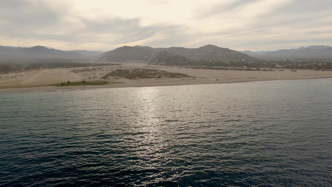 Calm ocean before a sandy beach and distant mountains