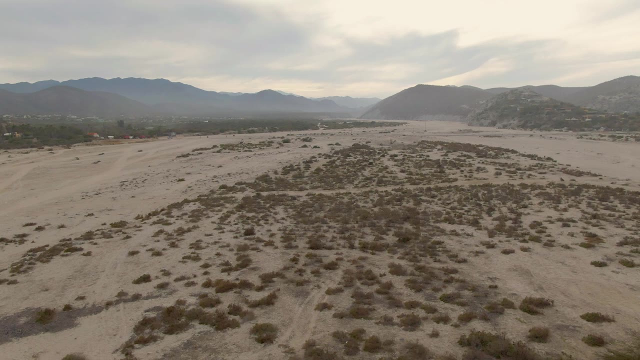 Open sandy wash with low bushes and mountain ridges in the background.