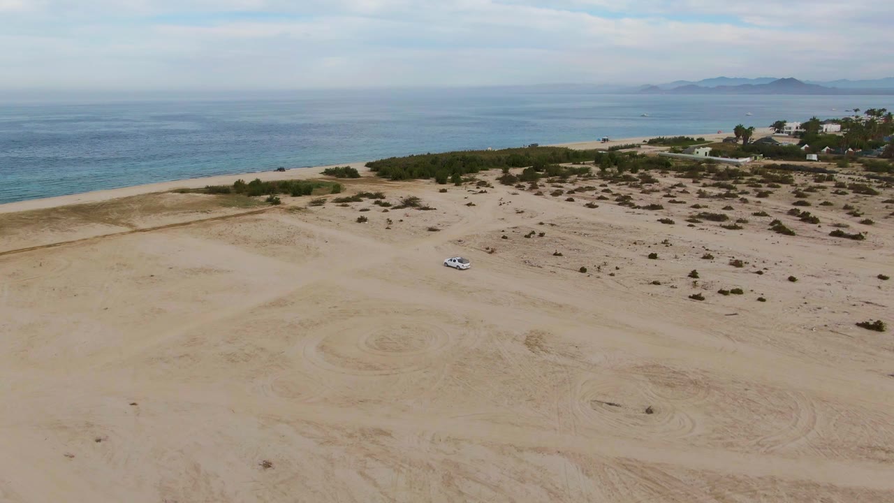 White car driving across open coastal sand
