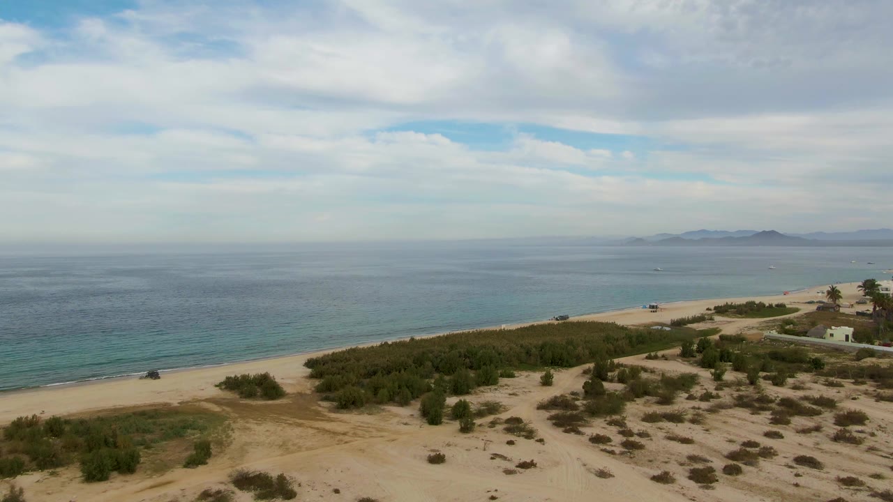 Sandy coastal scrub and beach road beside calm blue water.