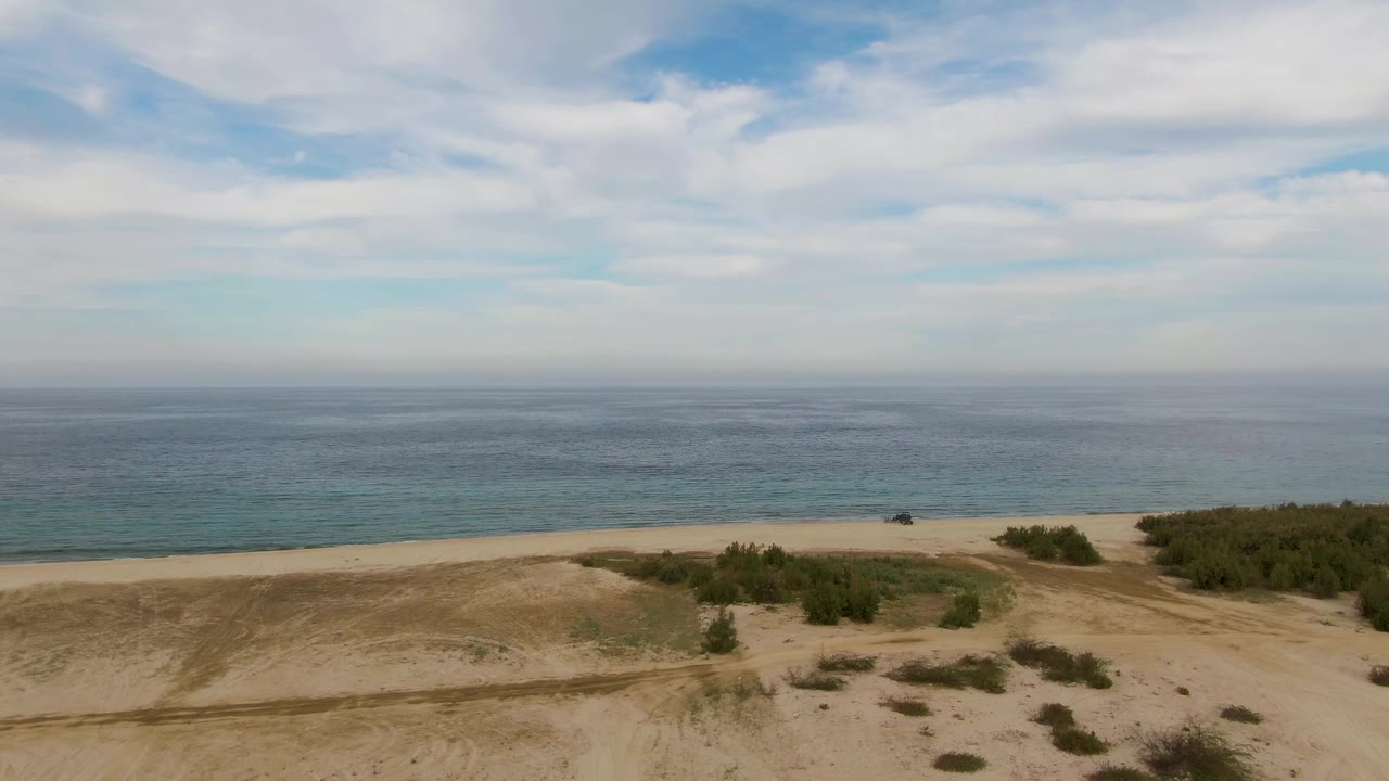 Mid-clip aerial frame over Los Barriles dunes and scrub vegetation with the beach and ocean stretching across the background, with no visible people.