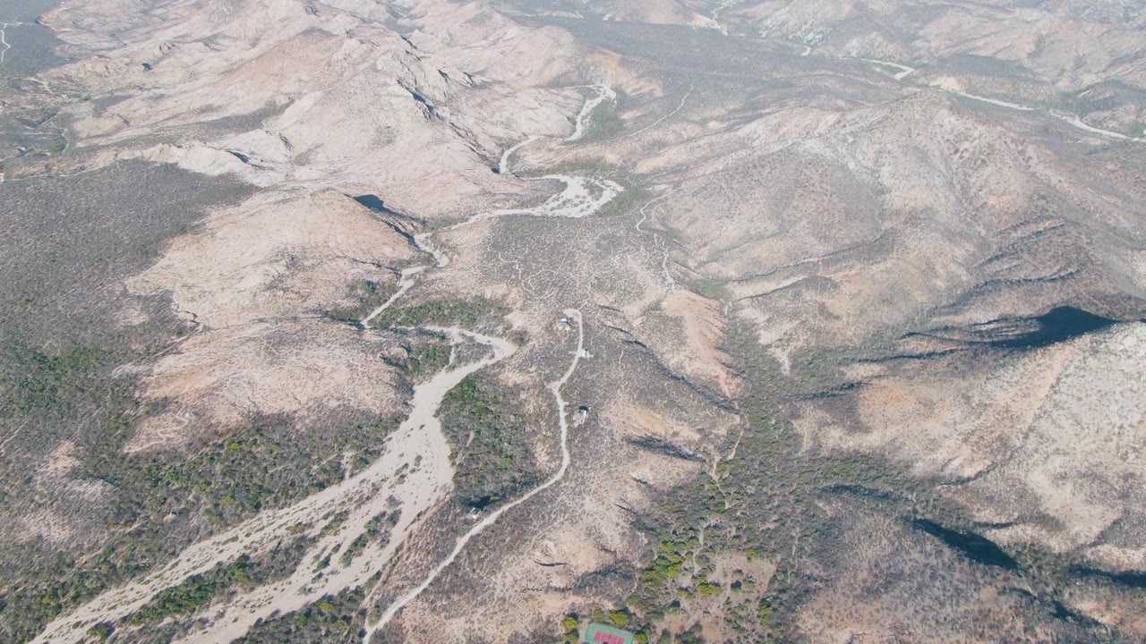 Second frame shows Cabo Pulmo arid hills from above, with pale road cuts running through scrub vegetation and the vehicle slightly farther along the lower road, with no visible people.