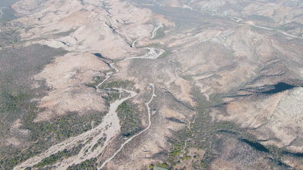 Aerial landscape of dry mountain terrain with dirt roads and a small vehicle at the lower edge.