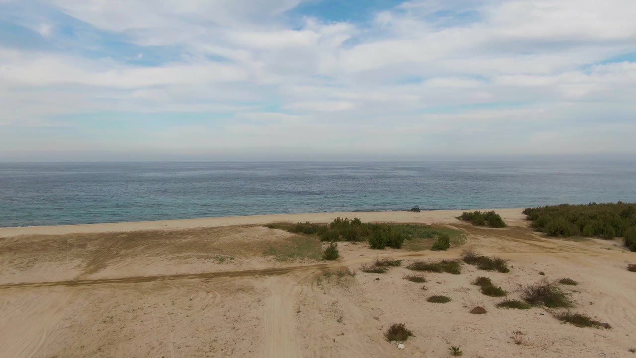 Sandy dunes with shrubs facing a blue ocean under clouds