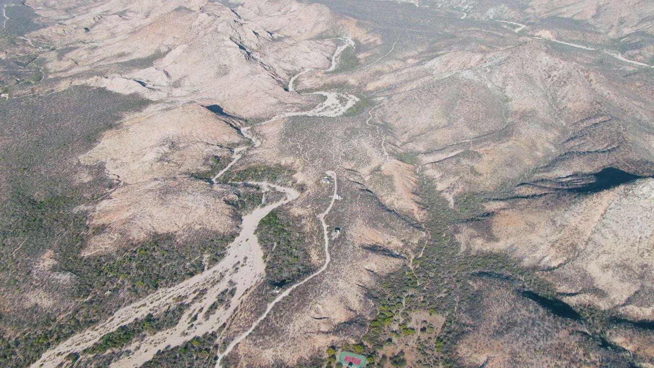 Drone-style view over Cabo Pulmo dry hills, with a winding pale road crossing scrubby terrain and no visible people in the frame.