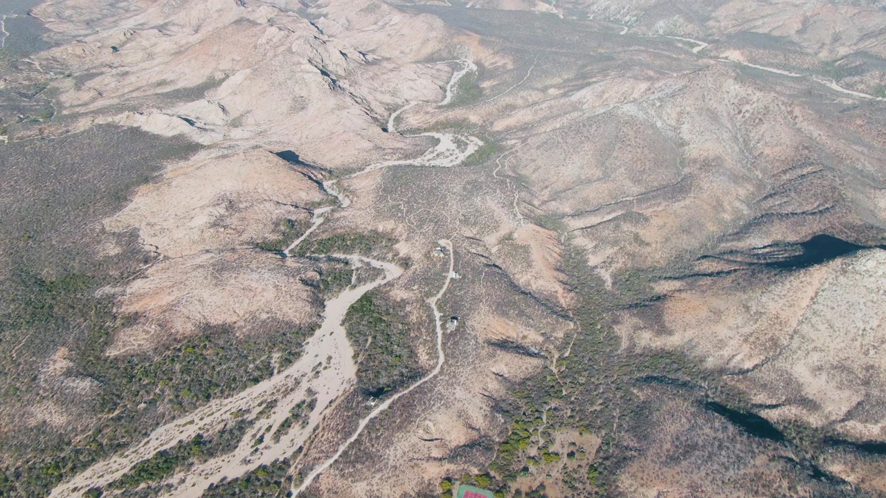 Dry hilly terrain with winding pale tracks and green patches.