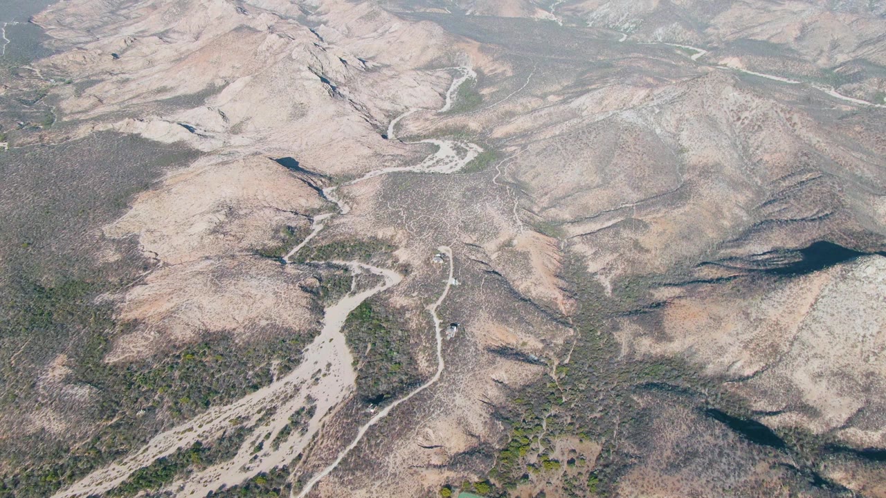 Oblique aerial view of Cabo Pulmo hills with pale exposed earth, darker ravine shadows, sparse vegetation, and no visible people.