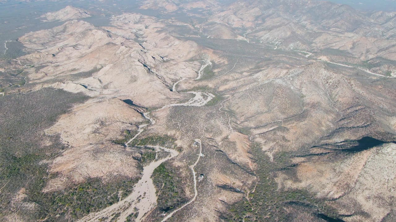 Aerial view of dry rocky mountains and pale riverbeds under a hazy sky.