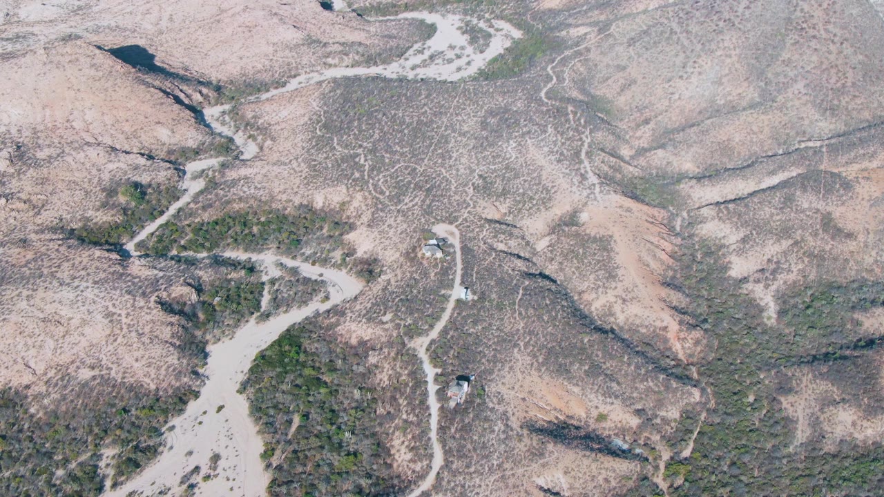 Aerial view of dry mountain slopes with pale winding trails and sparse shrubs.