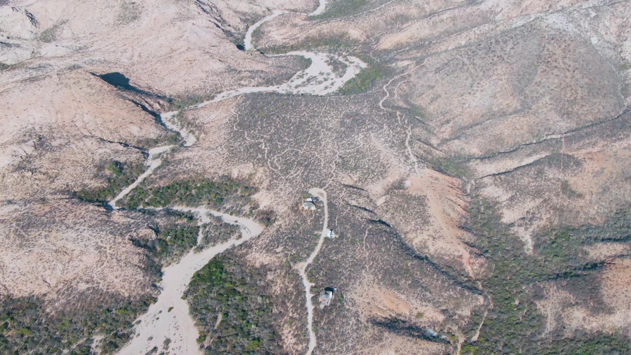 High aerial view in Cabo Pulmo showing beige ridges, dry washes, winding dirt trails, scattered shrubs, and no visible people.