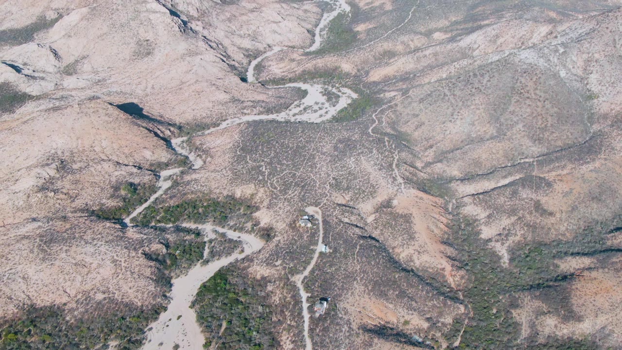 Aerial frame over Cabo Pulmo rocky desert slopes, where pale tracks curve through low green vegetation and no people are visible.
