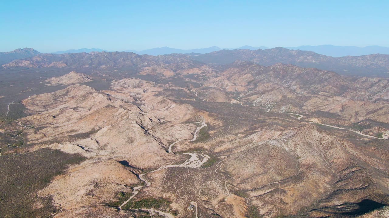 Wide aerial view over Cabo Pulmo desert ridges in Baja California Sur, with pale dirt roads crossing brown hills and no visible people.