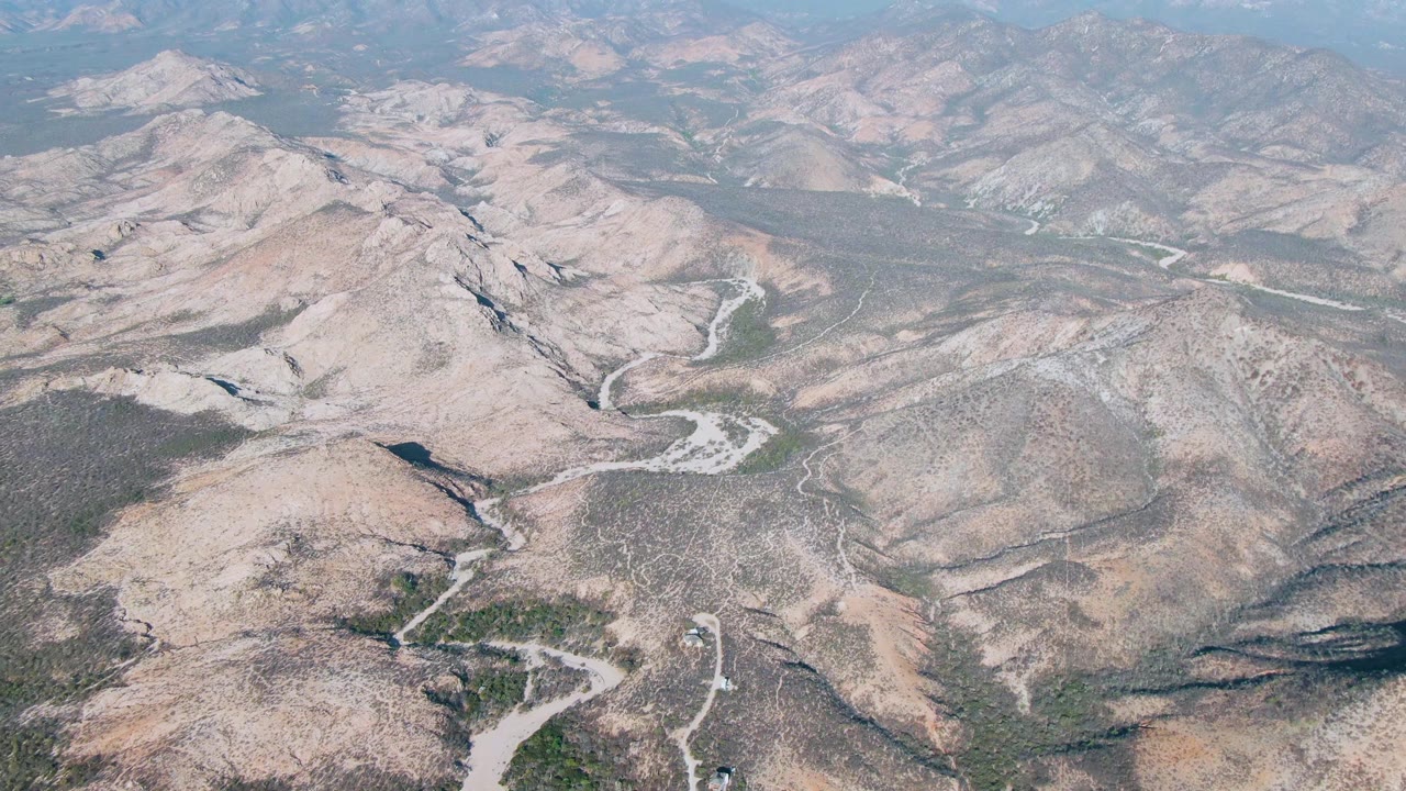 Drone-height view across Cabo Pulmo East Cape mountain ridges, with pale dry wash channels cutting through scrubland and no visible people.
