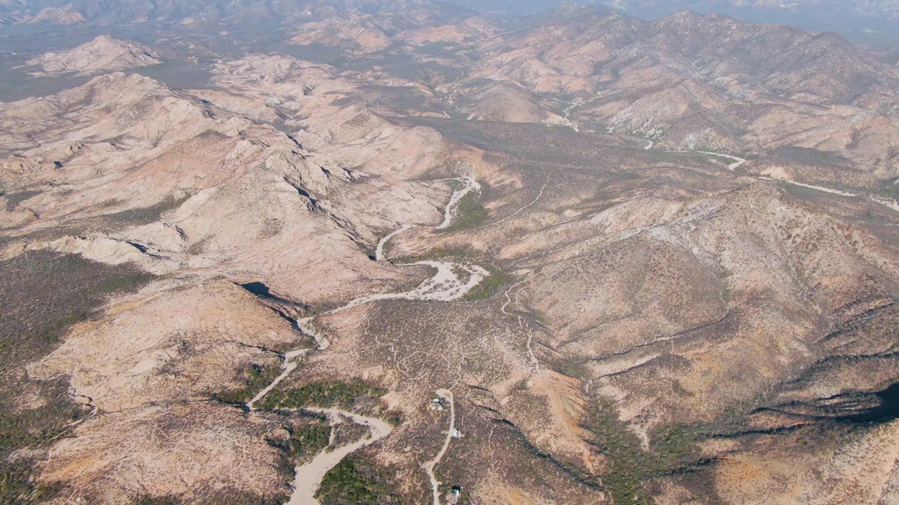 Drone view of tan mountain slopes crossed by curving dirt roads